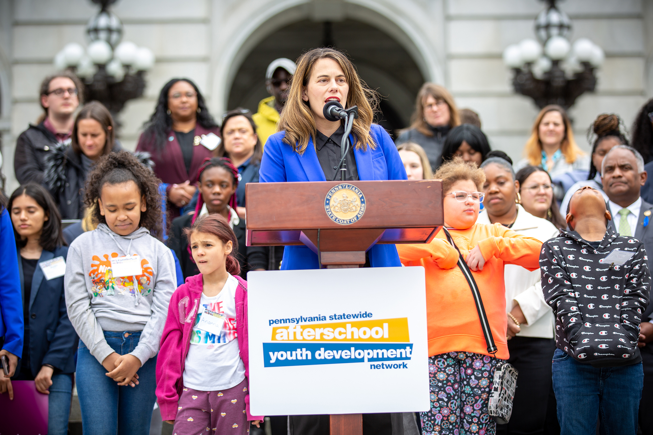 Representative Elizabeth Fiedler addressing attendees of rally, on Capitol steps. Group of students standing behind her.