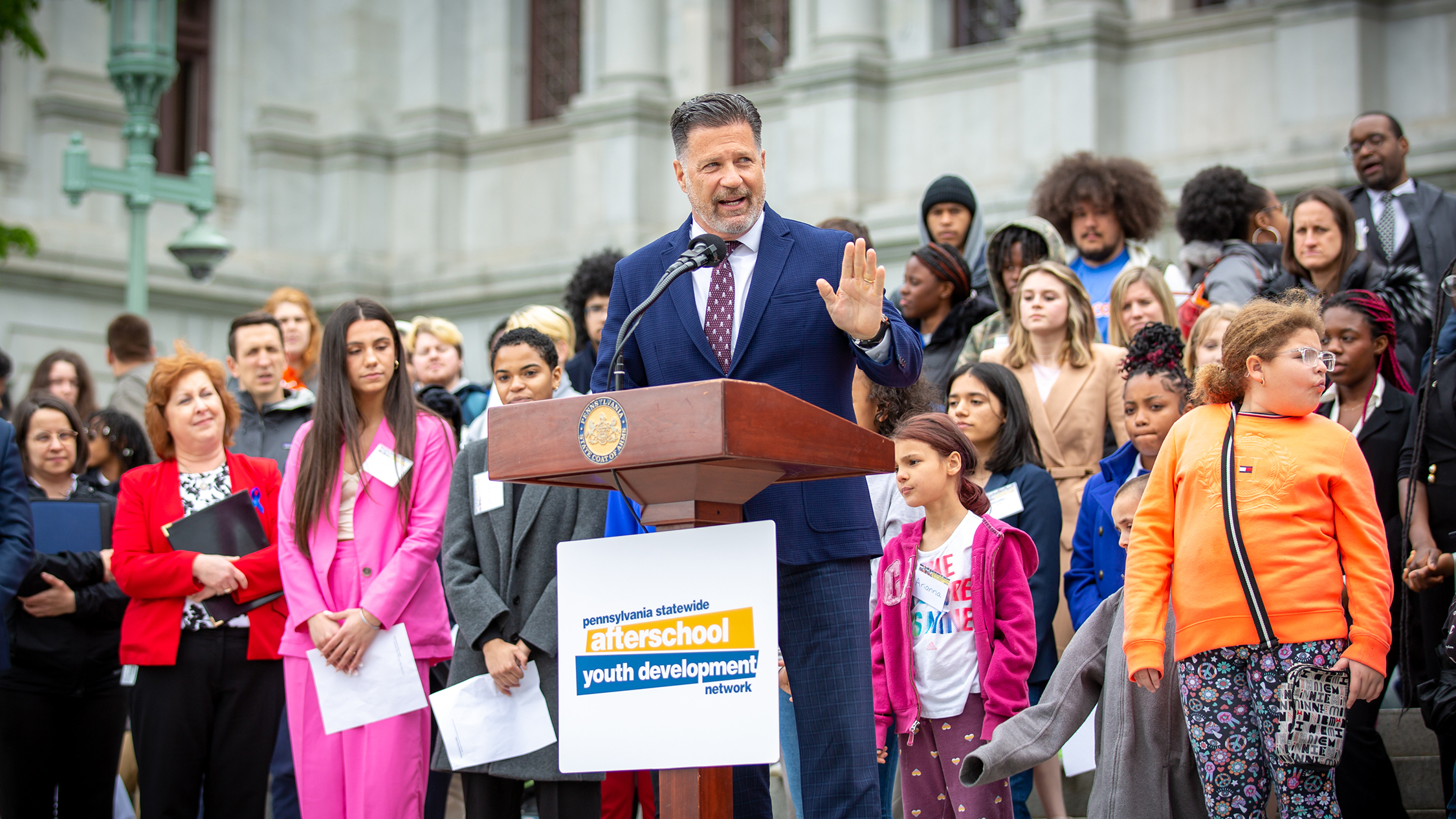 Senator Mike Regan speaking to attendees, with group of students and afterschool leaders standing behind him, on Capitol steps